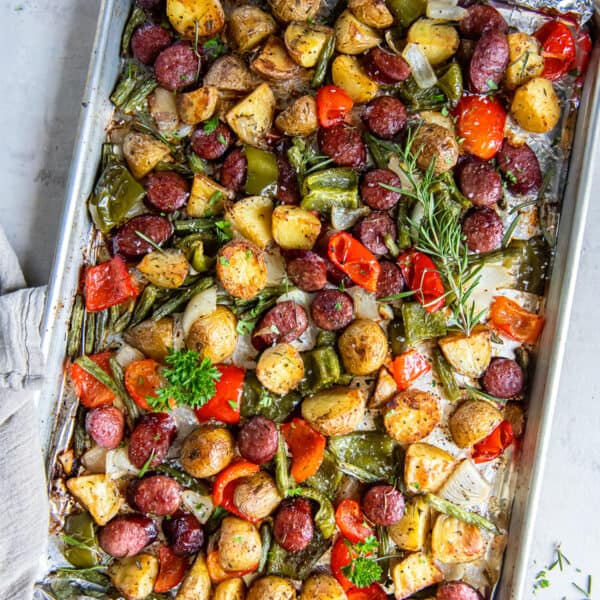 Sausage and potatoes with bell peppers and green beans on a baking sheet.