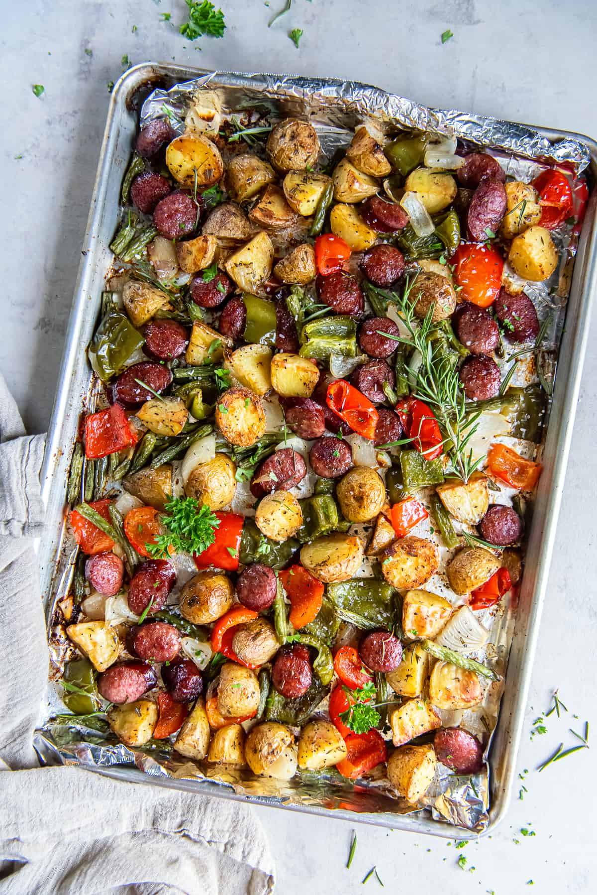 Sausage and potatoes with bell peppers and green beans on a baking sheet.