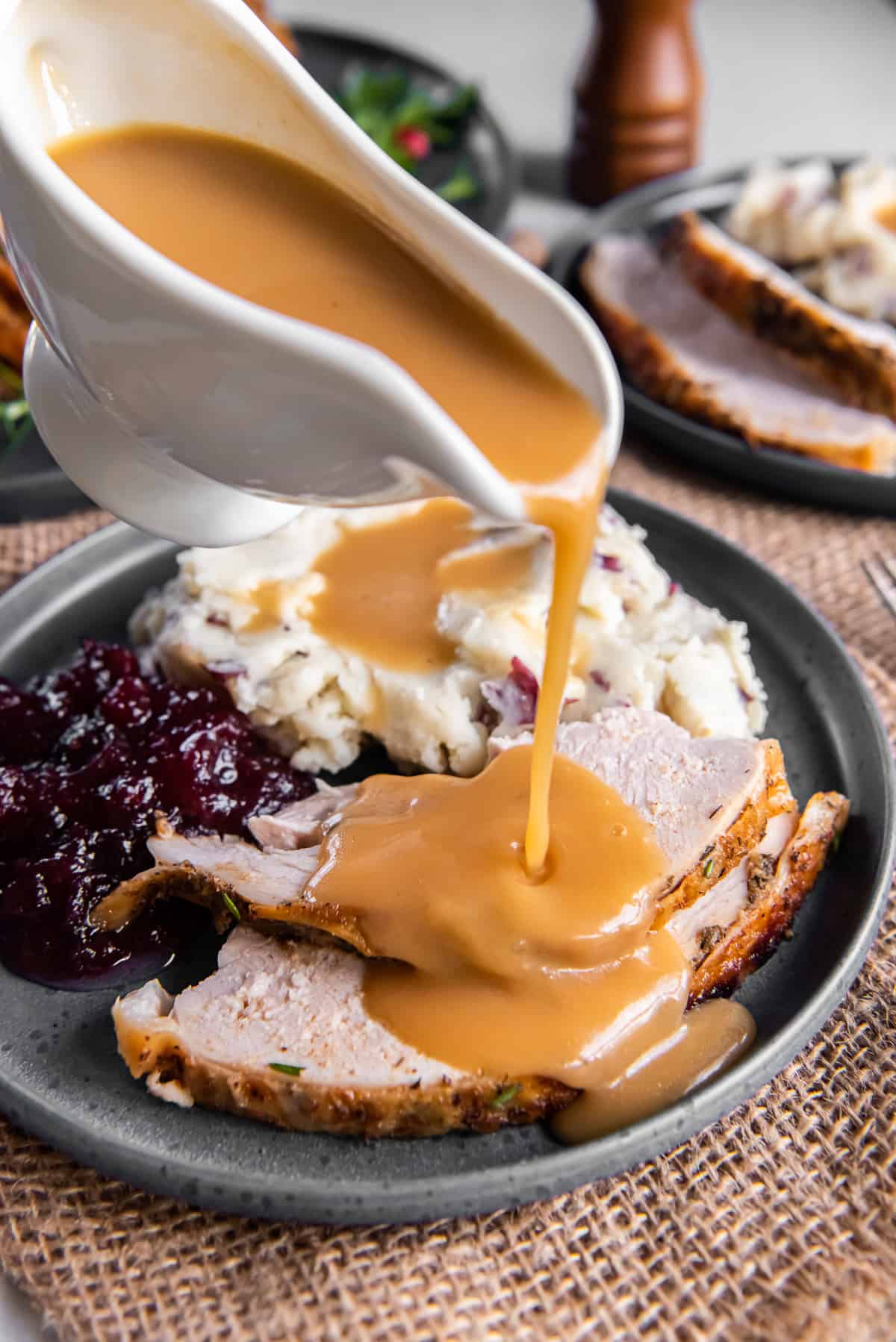 Slow cooker turkey gravy pouring from a gravy boat over slices of turkey on a plate.