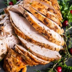 A top down shot of a sliced turkey breast on a grey platter with cranberries and fresh herbs.