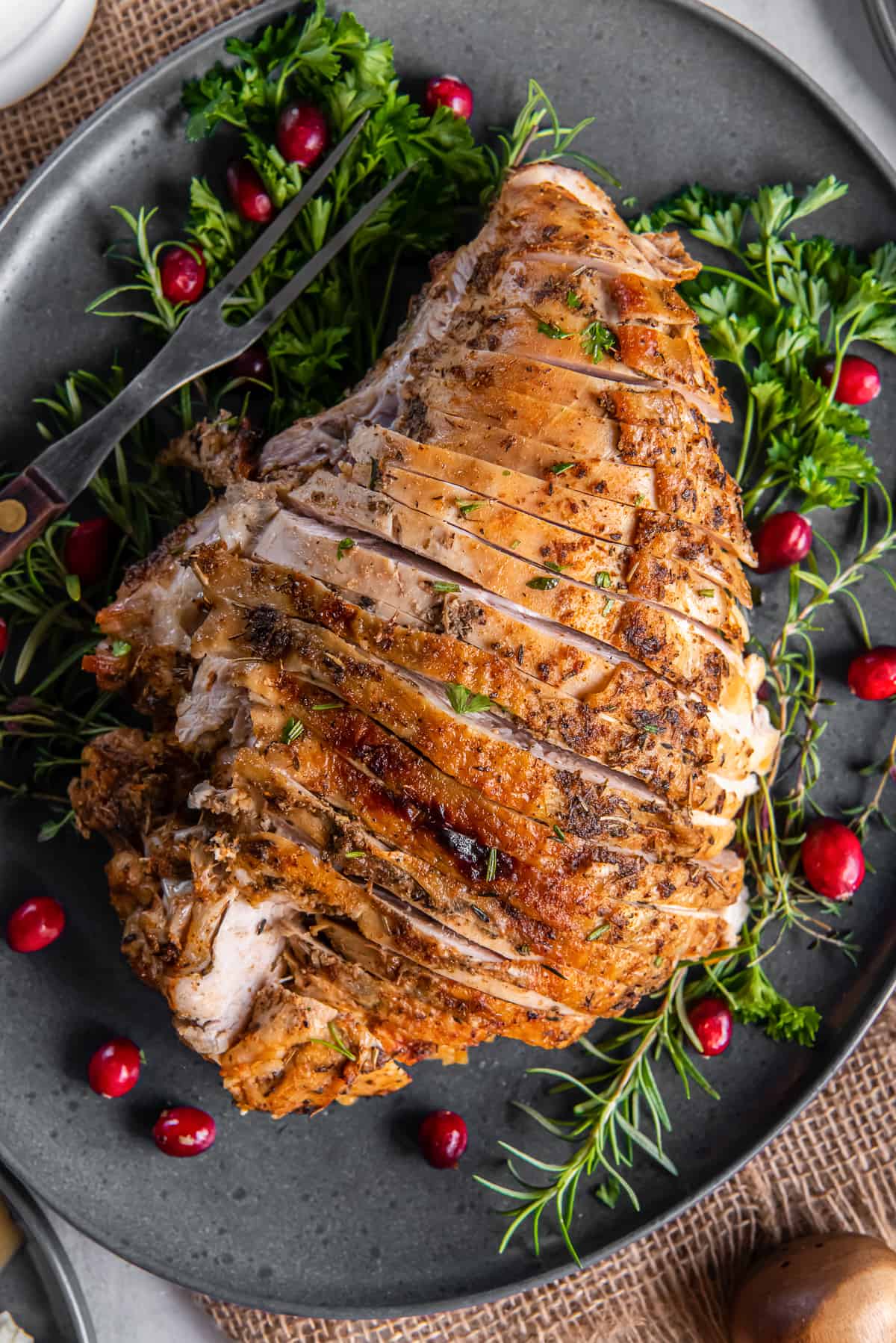 A top down shot of a sliced slow cooker turkey breast on a grey platter with cranberries and fresh herbs.