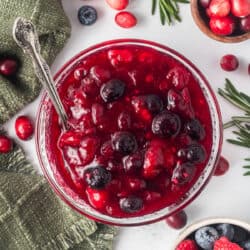 A top down shot of berry cranberry sauce in a glass bowl with a spoon.
