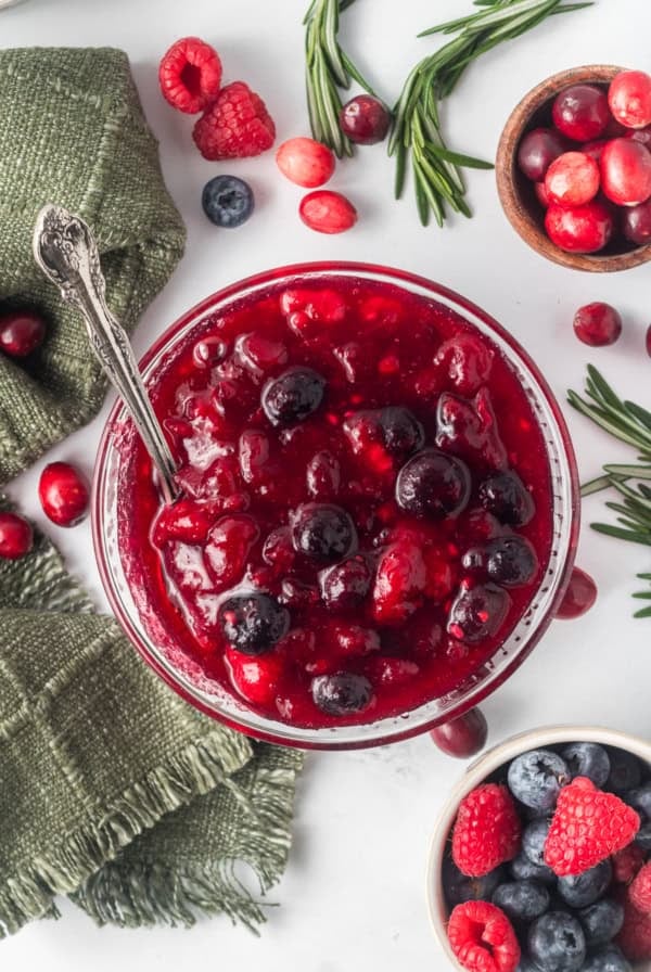 A top down shot of berry cranberry sauce in a glass bowl with a spoon.