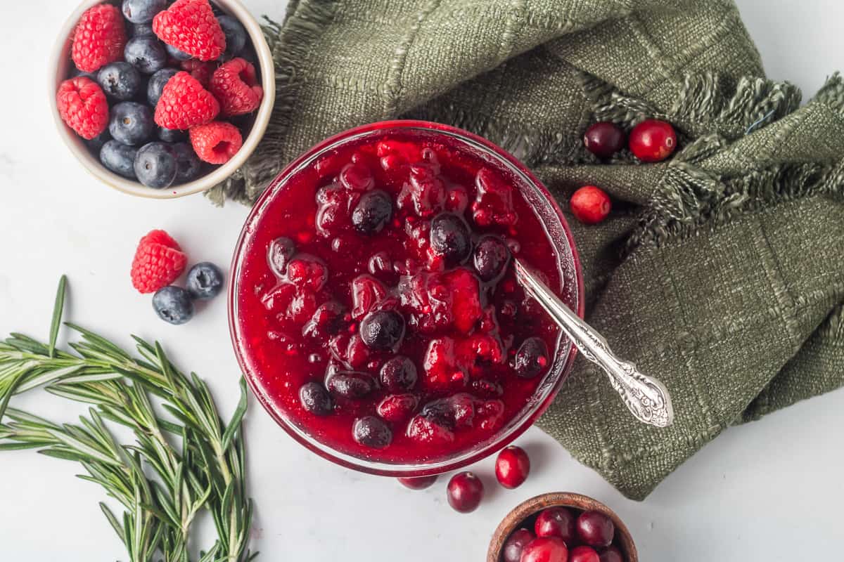 A top down shot of berry cranberry sauce in a glass bowl with a spoon.