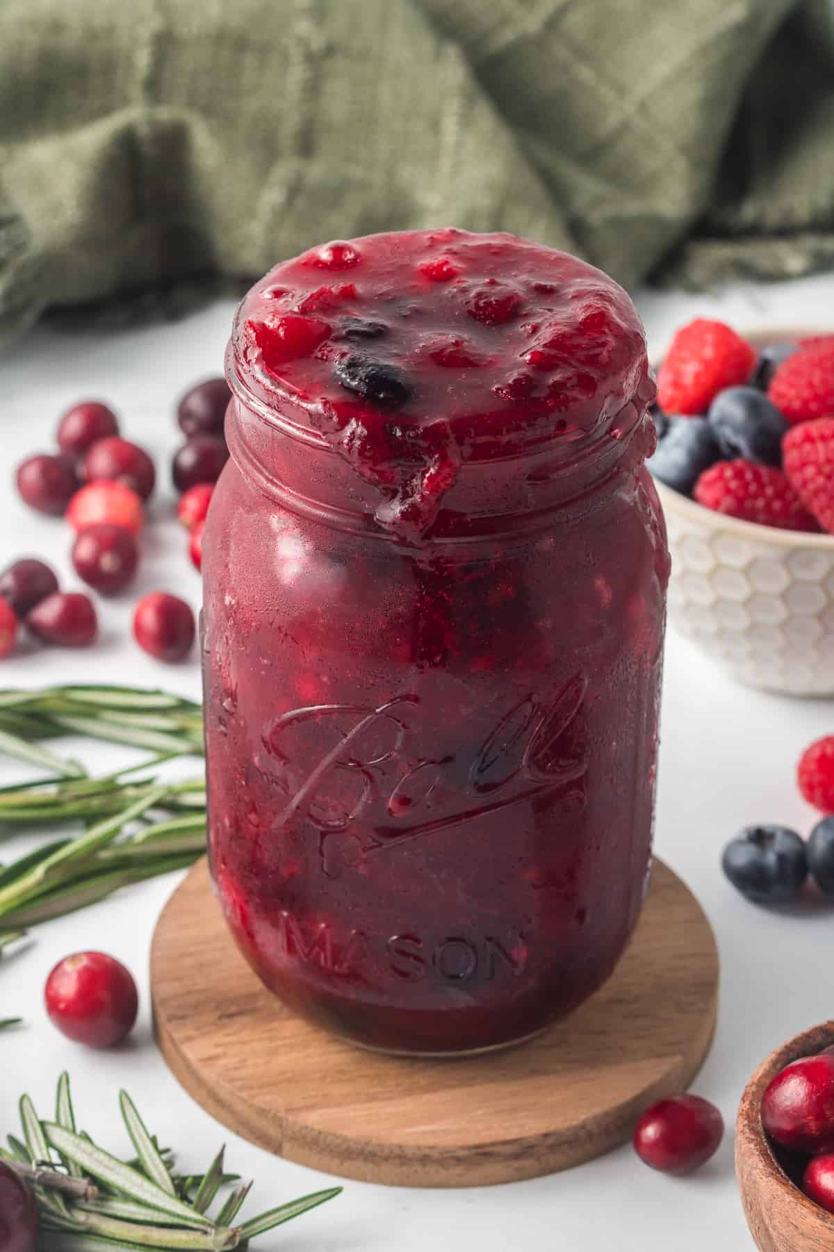 A mason jar filled with cranberry sauce with fresh berries.