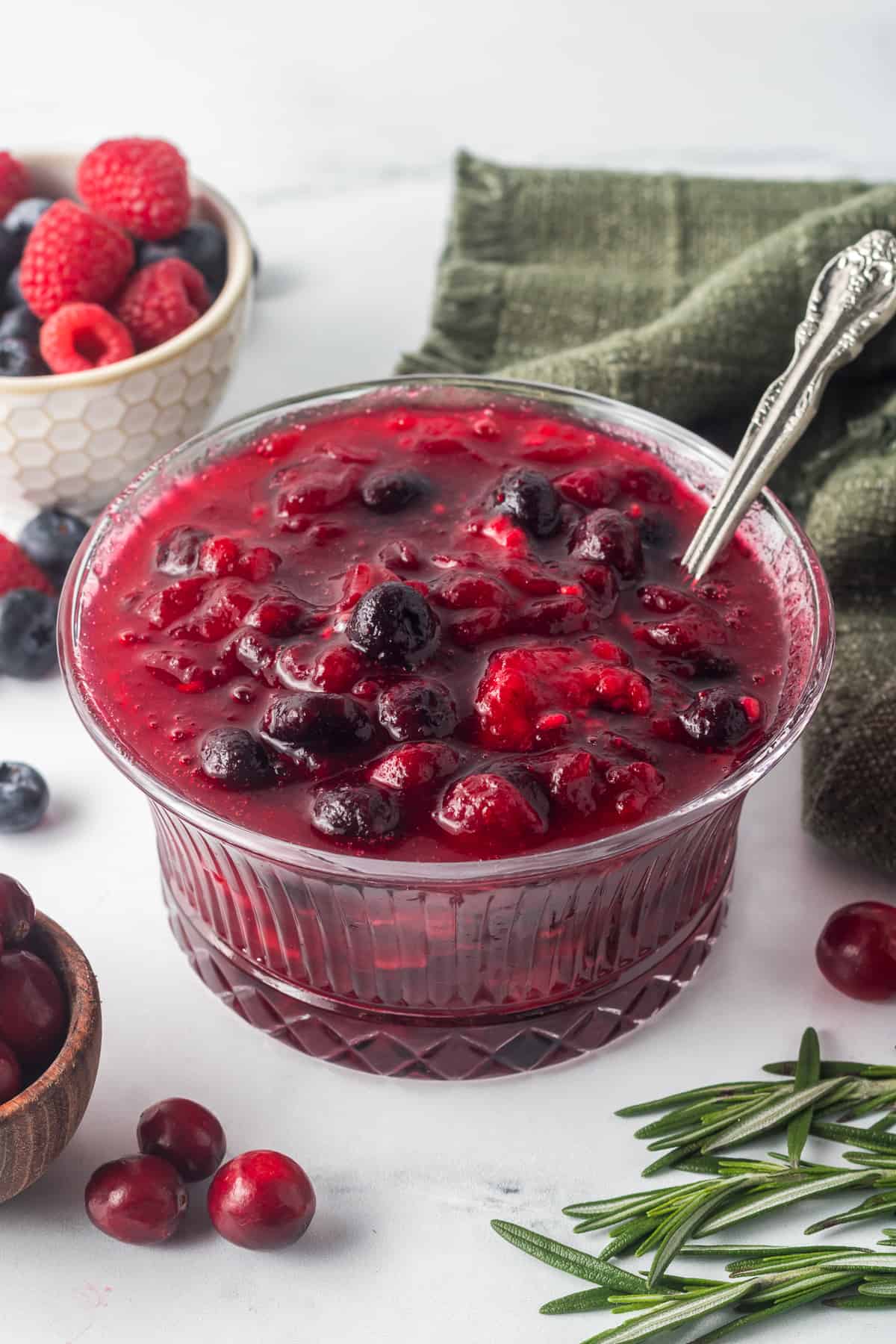 A spoon resting in a pretty glass serving dish filled with berry cranberry sauce.
