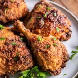 An air fried chicken drumstick and other pieces on a white plate with parsley.