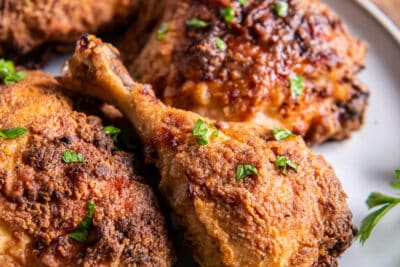 An air fried chicken drumstick and other pieces on a white plate with parsley.