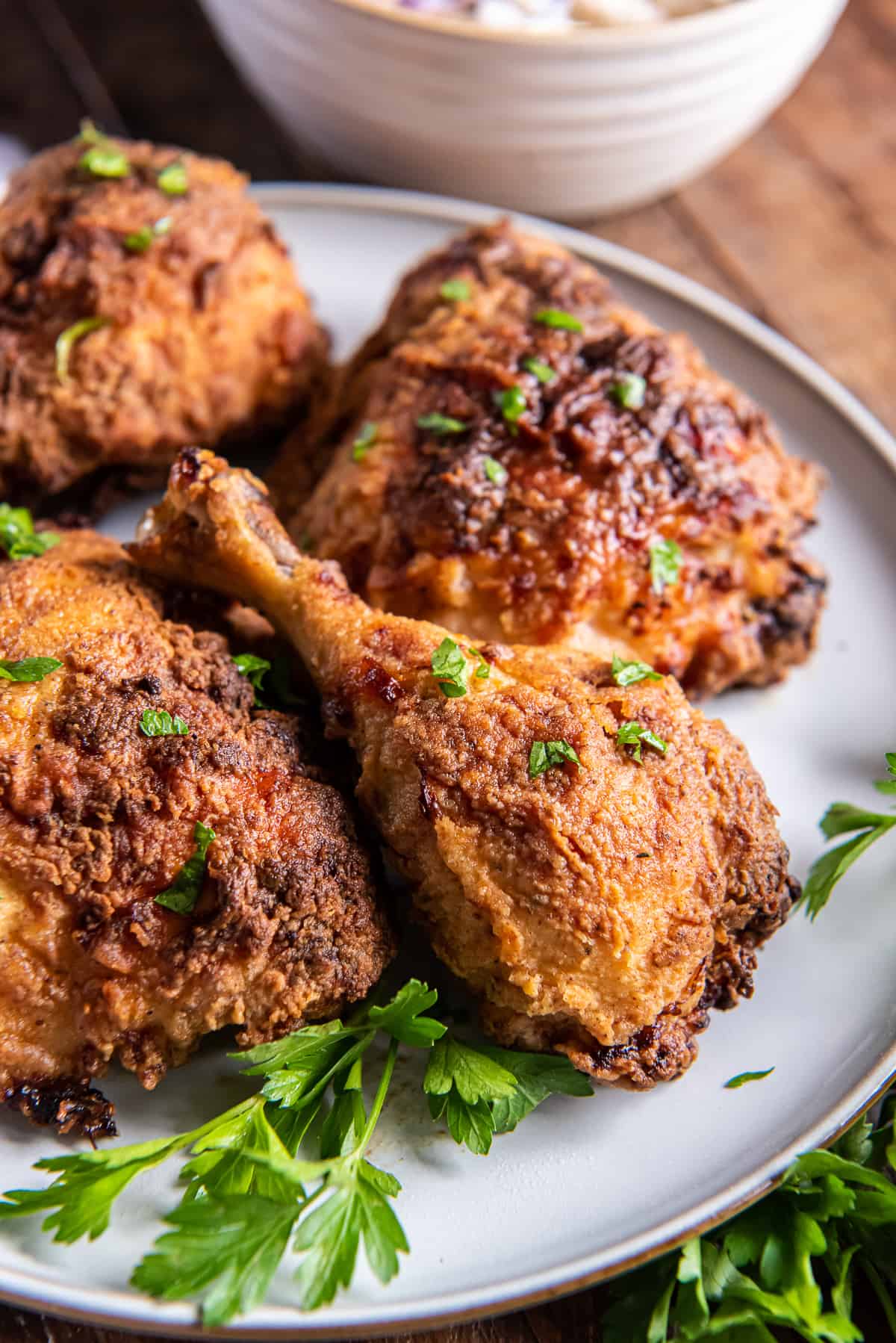 An air fried chicken drumstick and other pieces on a white plate with parsley.