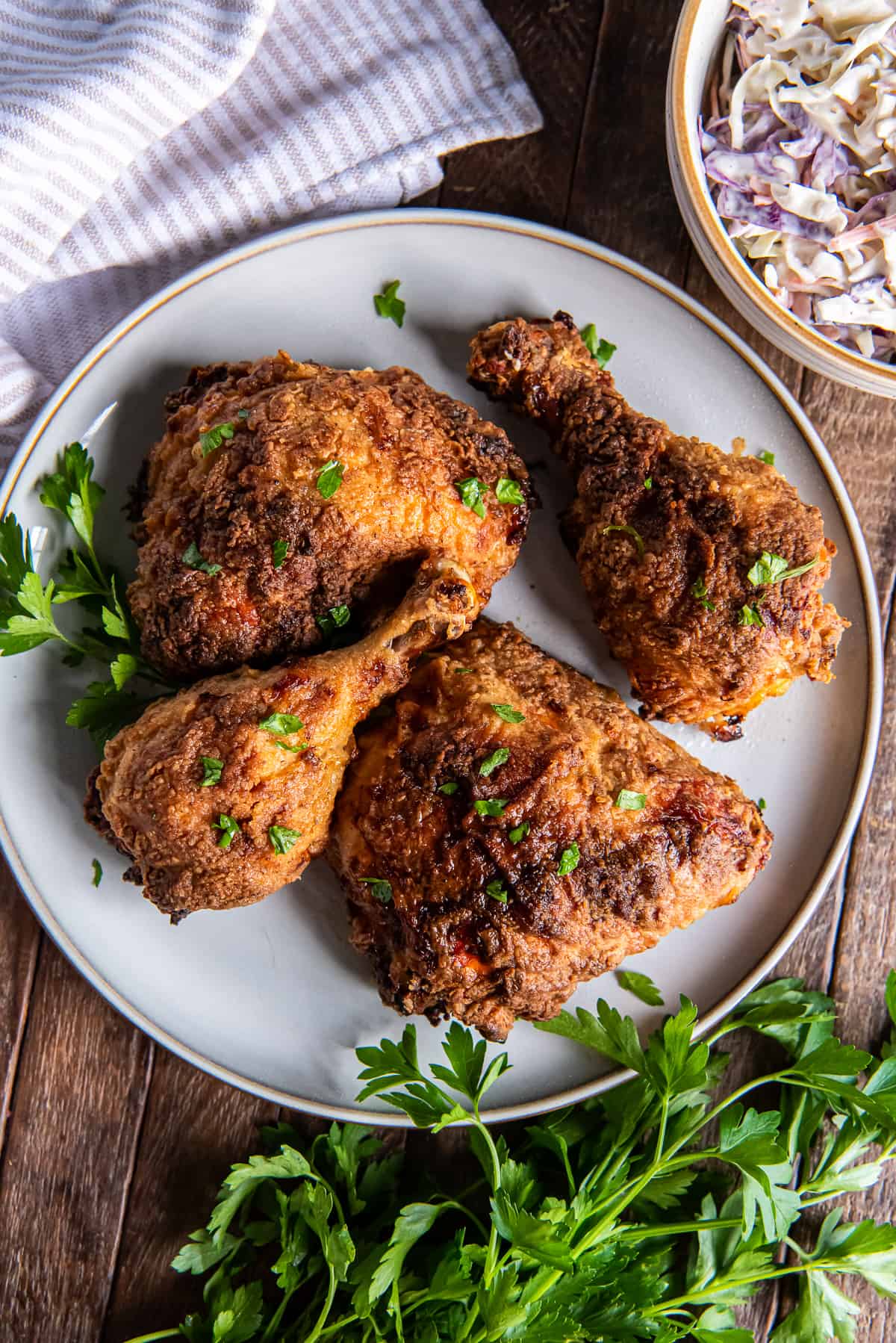 A top down shot of air fryer fried chicken on a white plate next to a bowl of coleslaw.