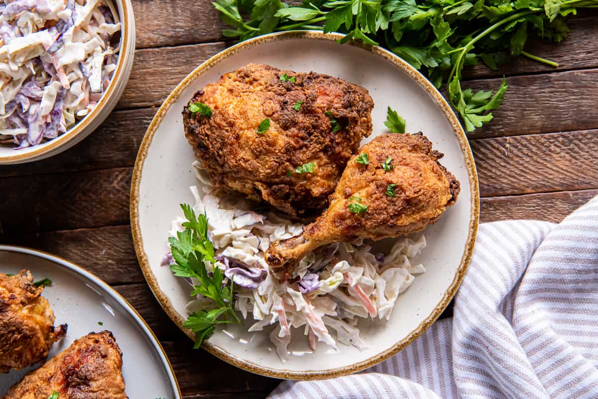 Two pieces of air fryer fried chicken on a dinner plate with coleslaw.