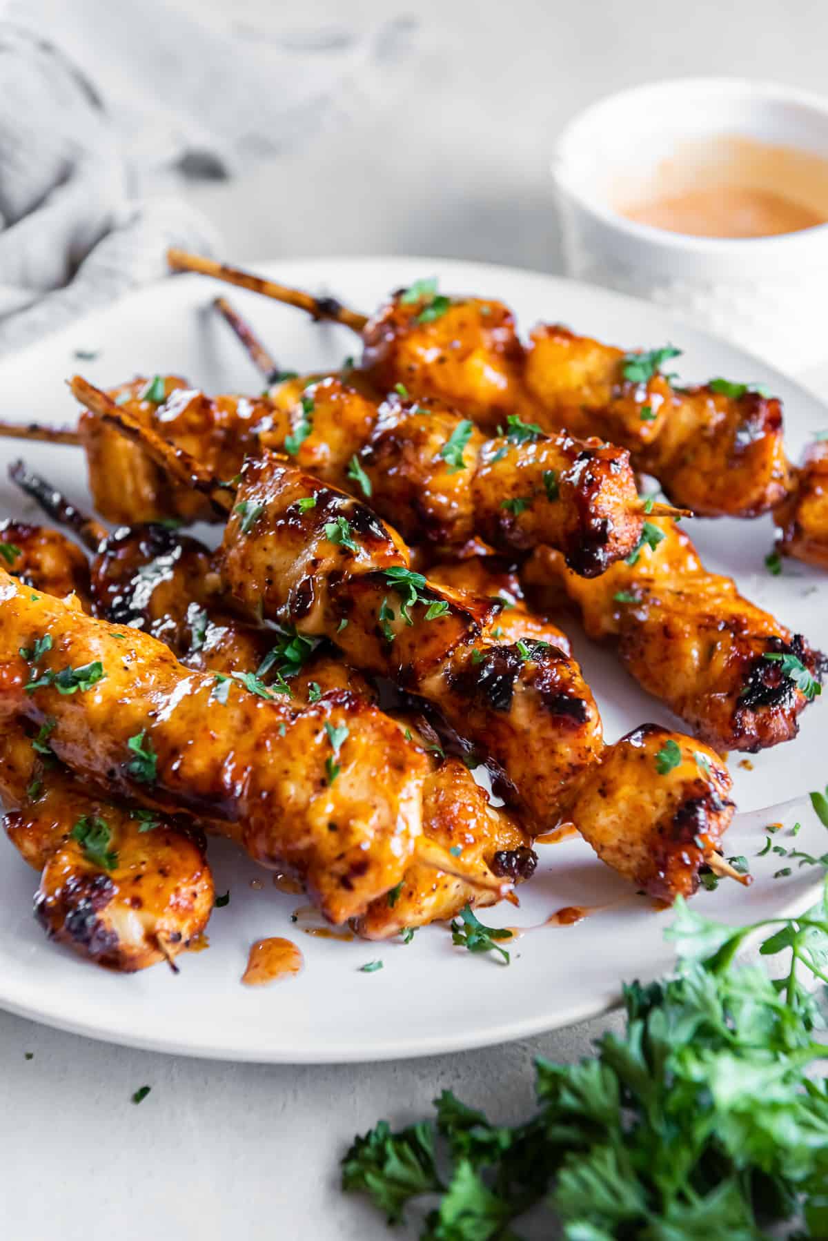 Bang bang chicken skewers on a white plate next to sprig of parsley.