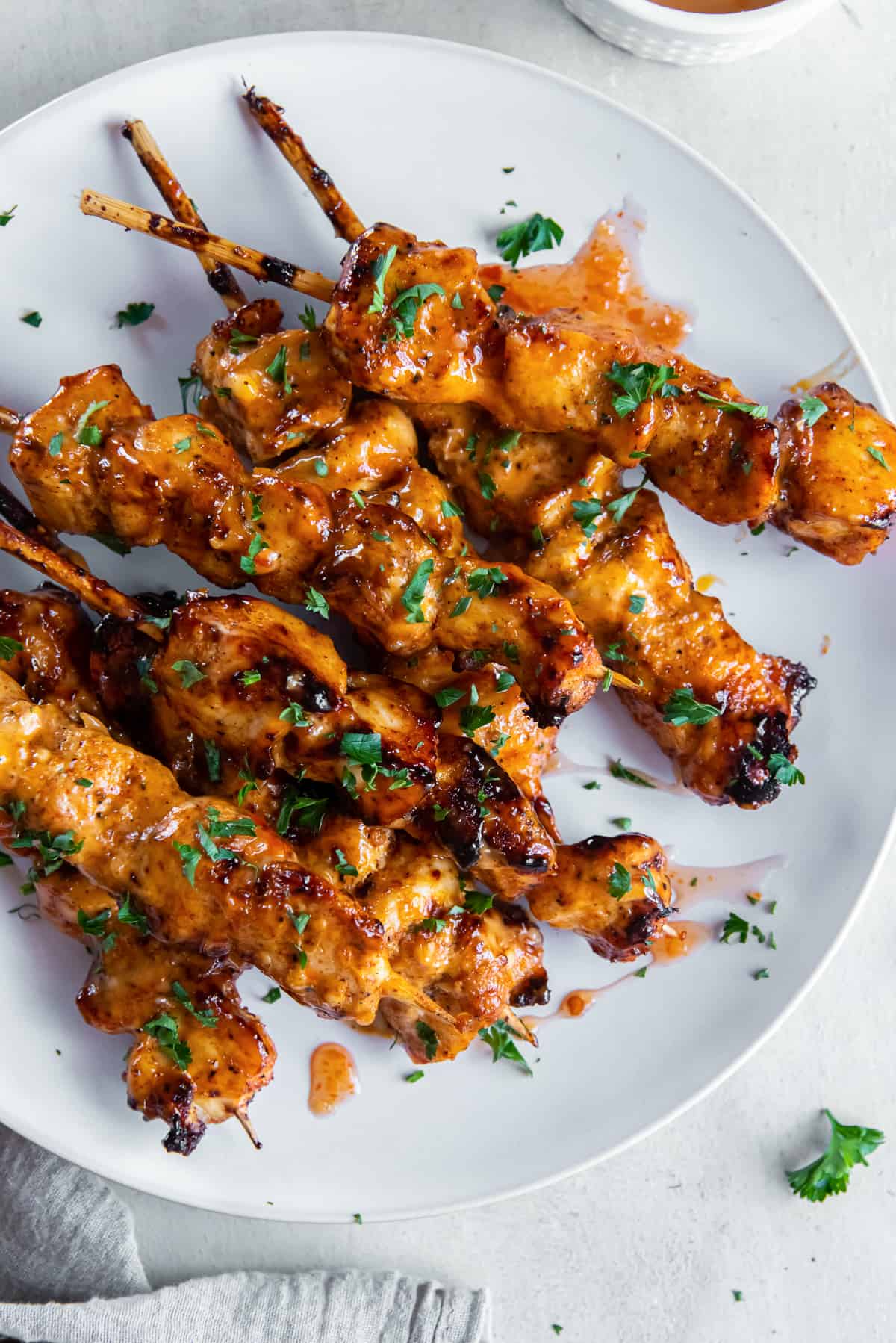 A top down shot of bang bang chicken skewers on a white plate next to a grey cloth,
