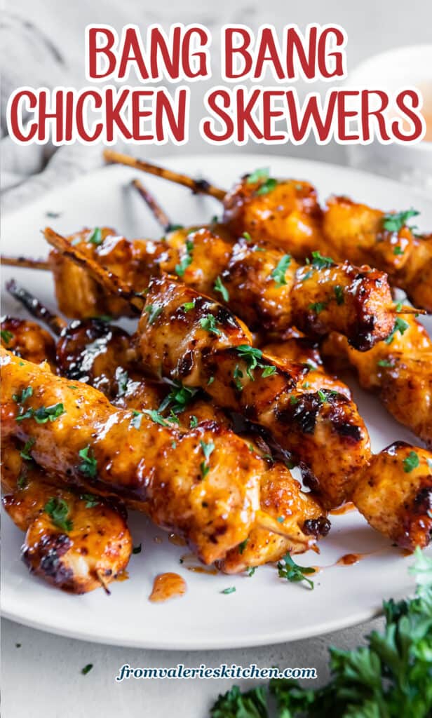 Bang bang chicken skewers on a white plate next to sprig of parsley with text.