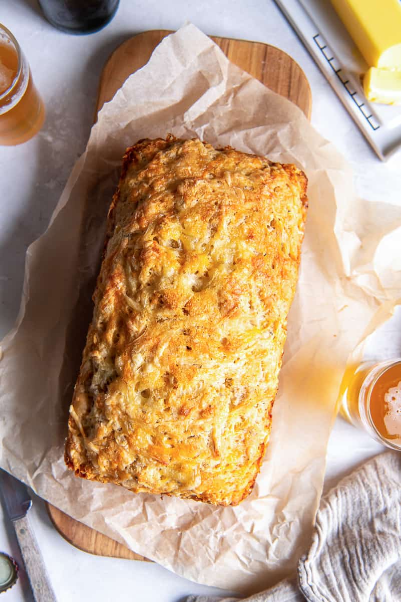 A top down shot of a loaf of cheese beer bread on a parchment paper lined board.