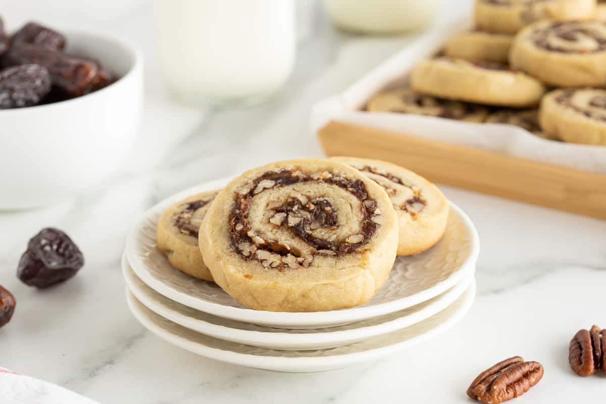 Three date pinwheel cookies on stack of small white plates.