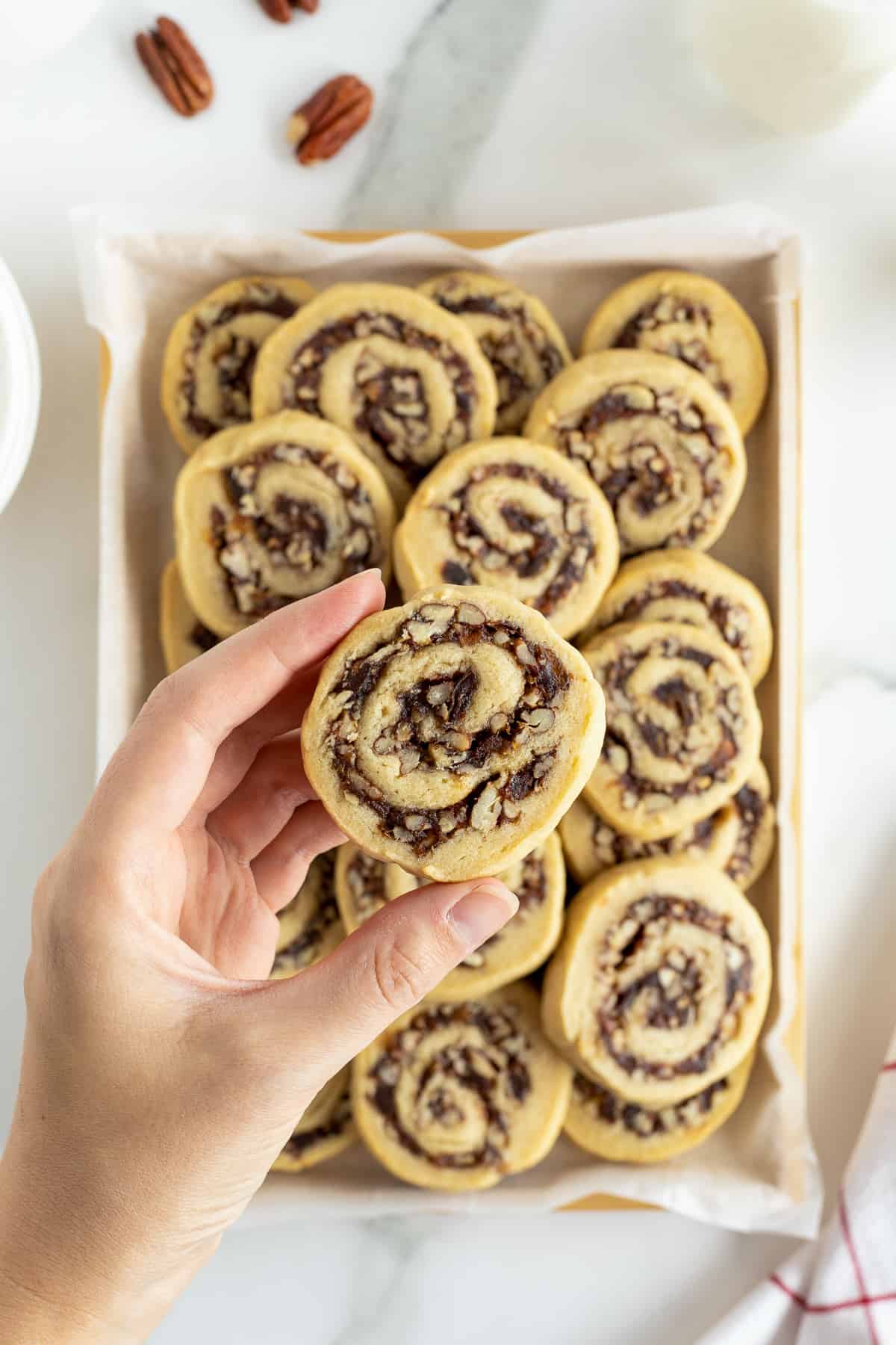 A hand holding a date pinwheel cookie over a platter of cookies.