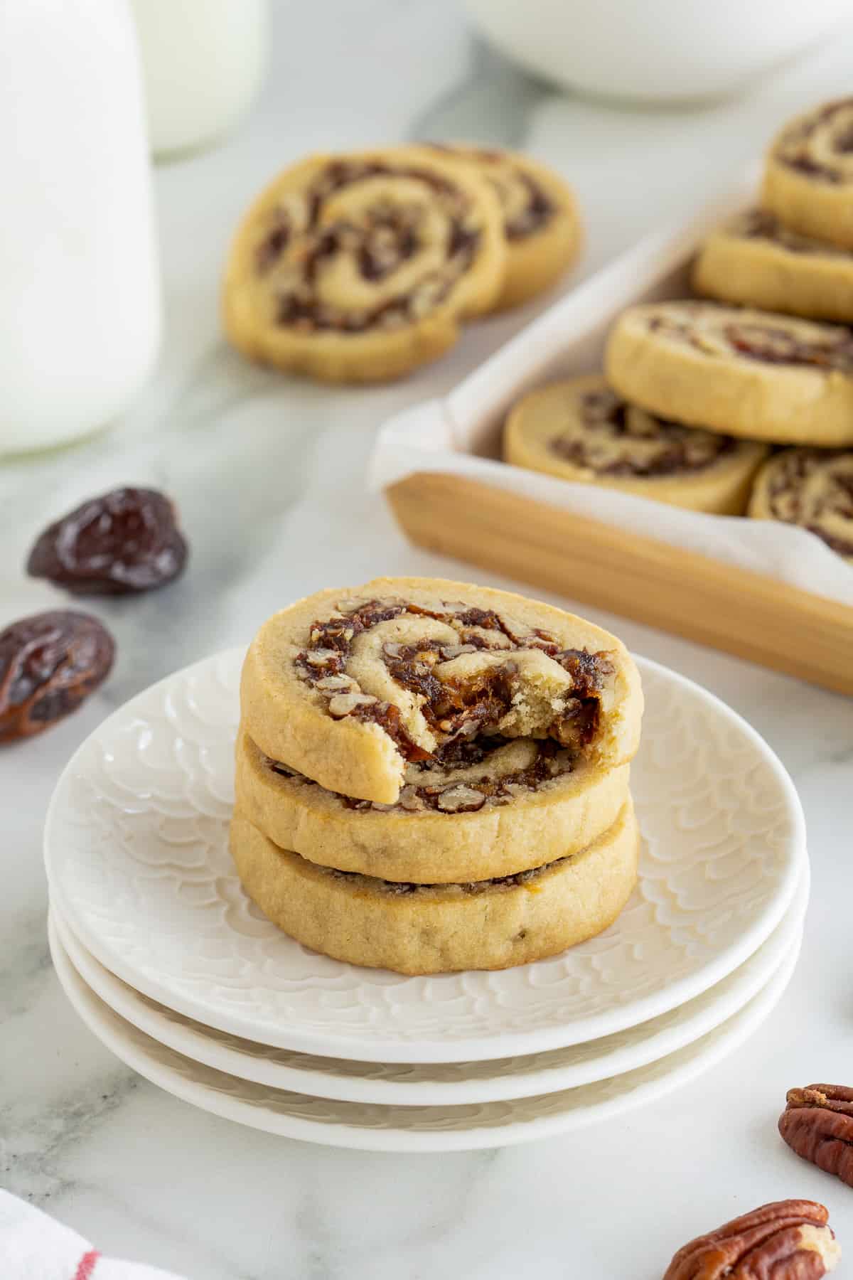 A date pinwheel cookie with a bite missing resting on top of two cookies on a stack of white plates.