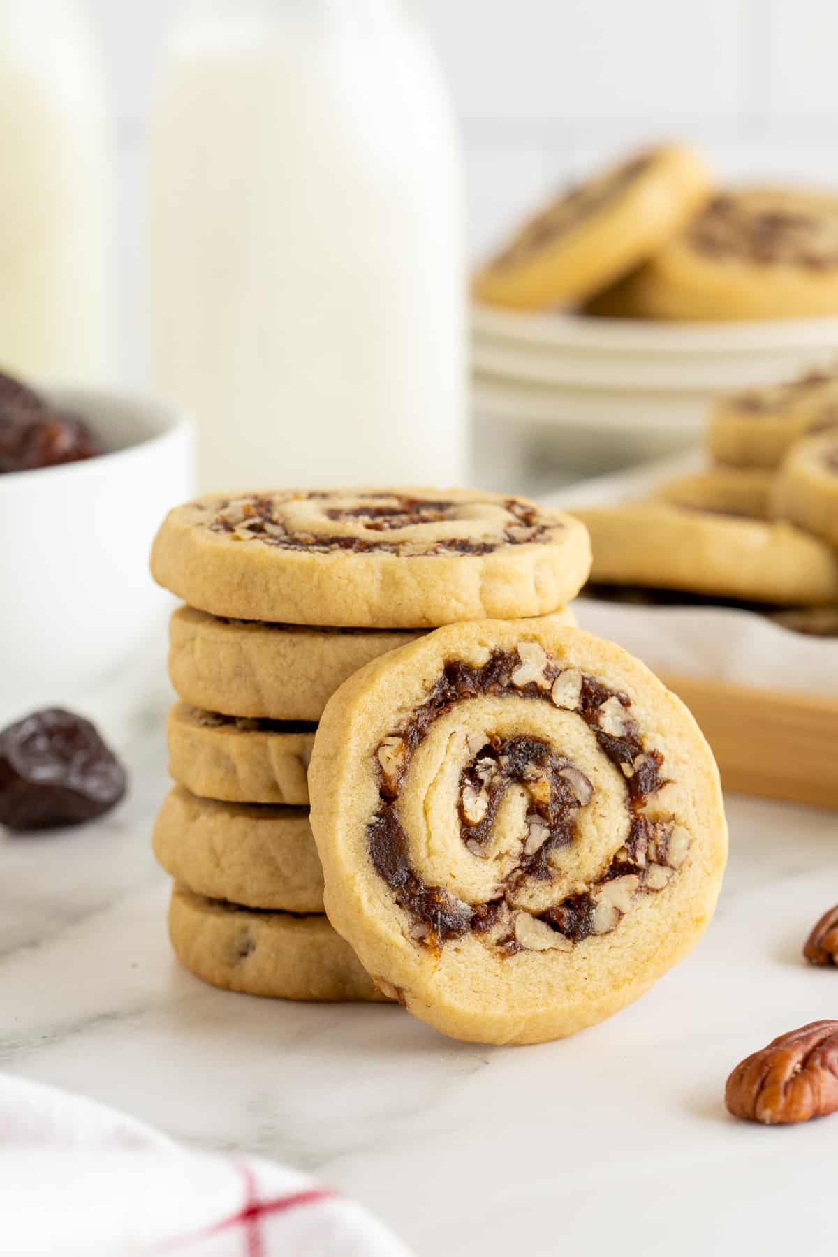 A date pinwheel cookie leaning against a stack of cookies on a kitchen counter.