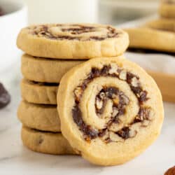 A date pinwheel cookie leaning against a stack of cookies on a kitchen counter.