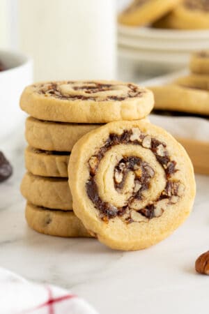 A date pinwheel cookie leaning against a stack of cookies on a kitchen counter.
