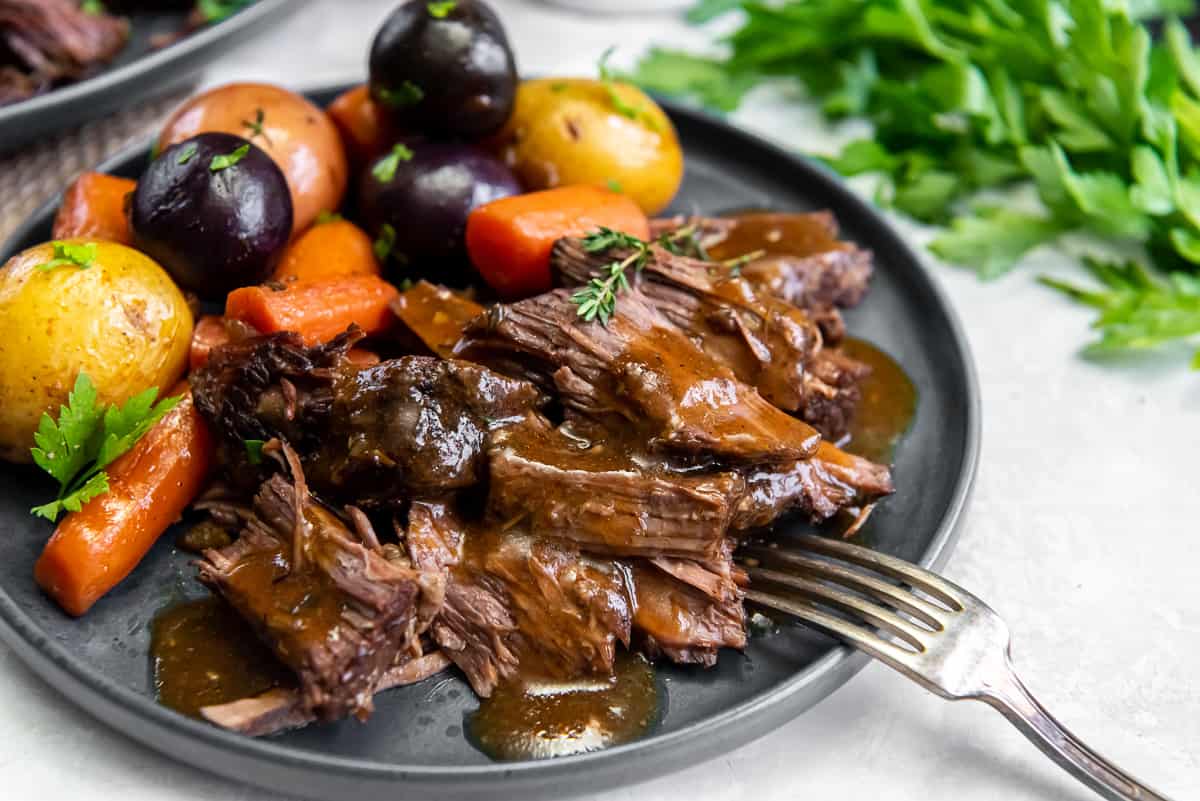 A fork resting on a dinner plate filled with pot roast and vegetables.