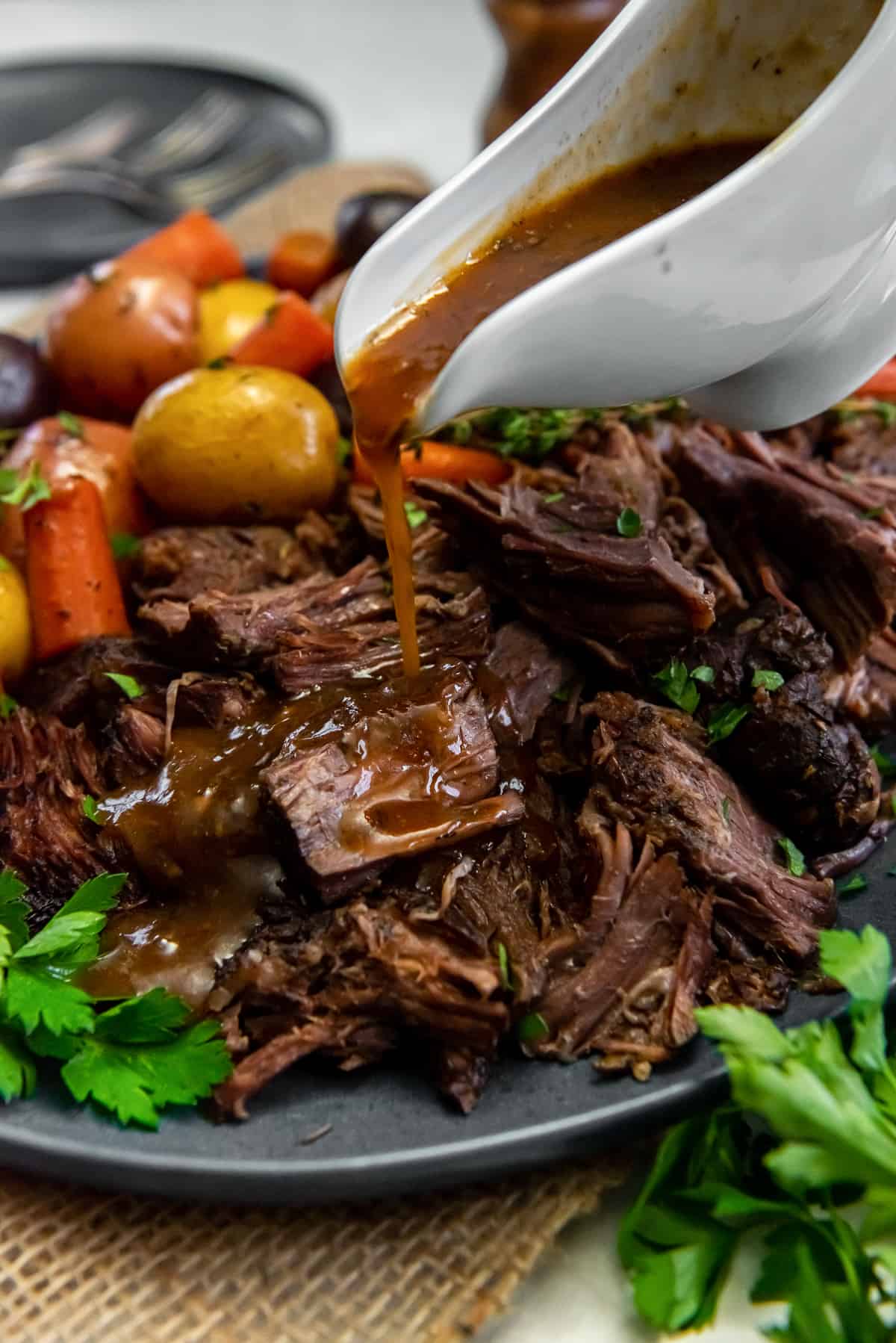 Gravy pouring from a gravy boat over pot roast on a platter.