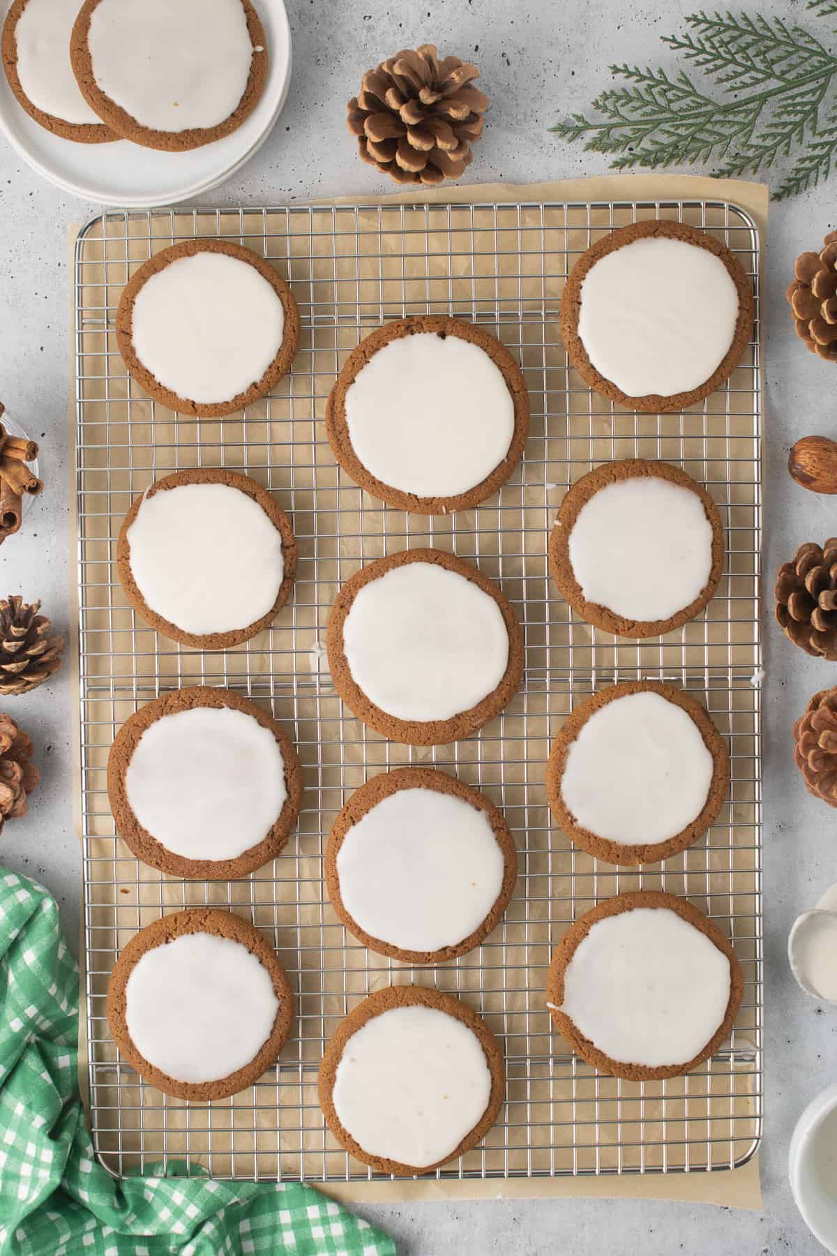 Iced molasses cookies on a wire rack surrounded by small pine cones and pine branches.