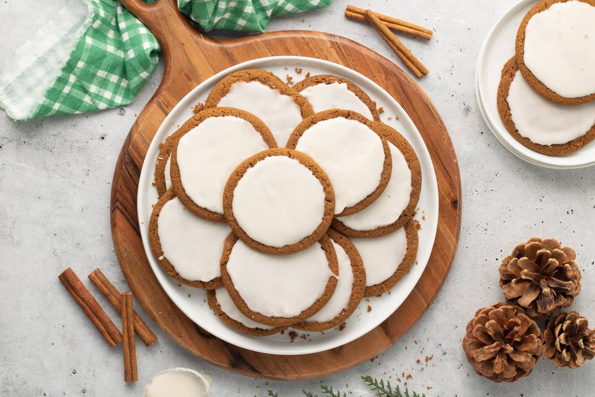 A top down shot of a plate of iced molasses cookies on a handled wood board.