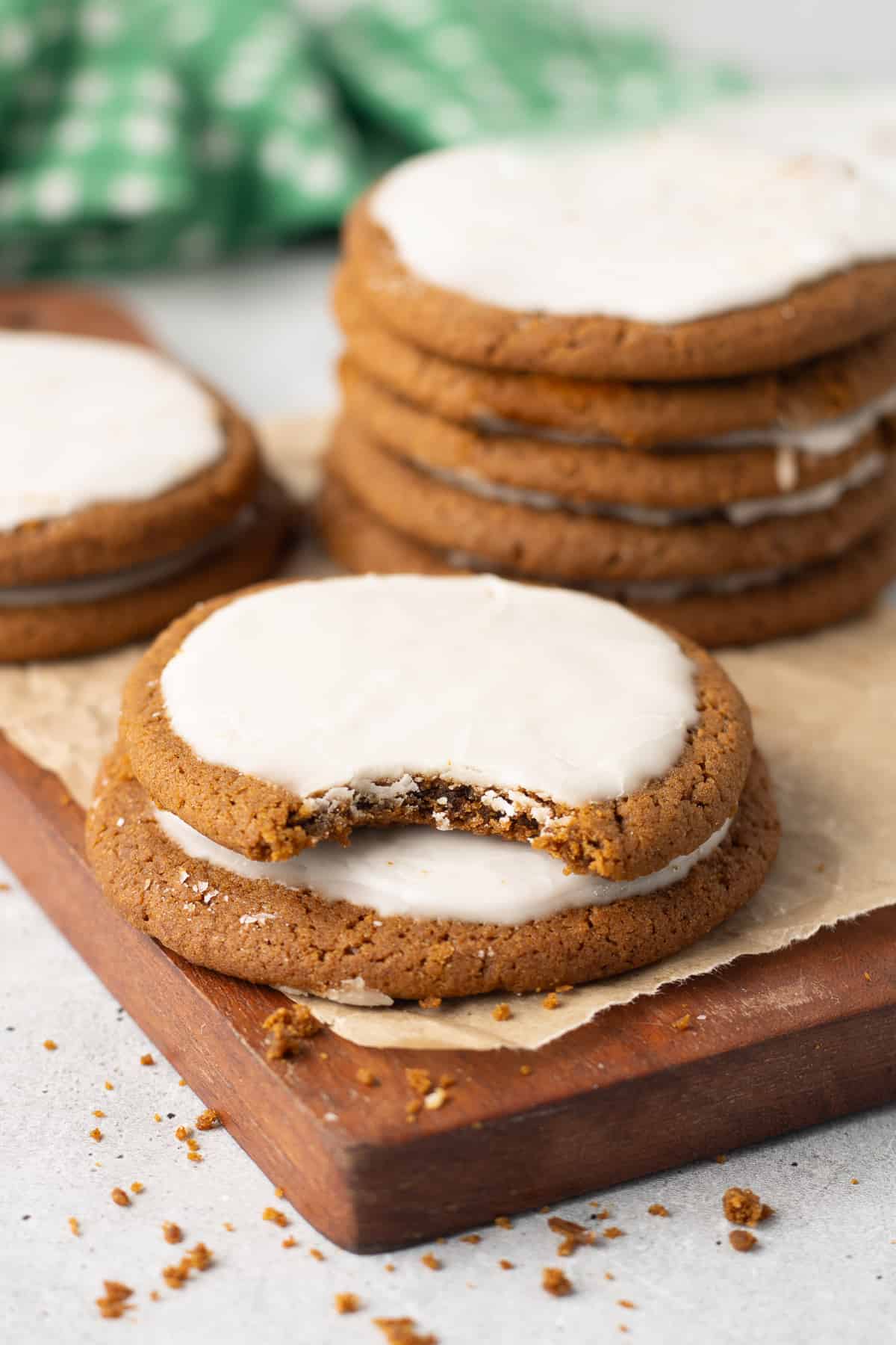 A molasses cookie with a bite missing stack on top  of another cookies on a wood board.