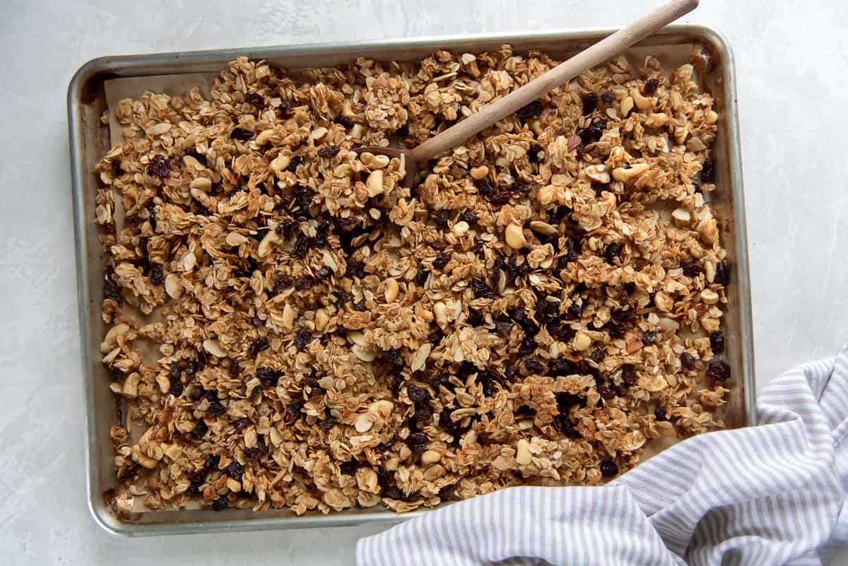 A top down shot of maple honey granola on a baking sheet with a wooden spoon.