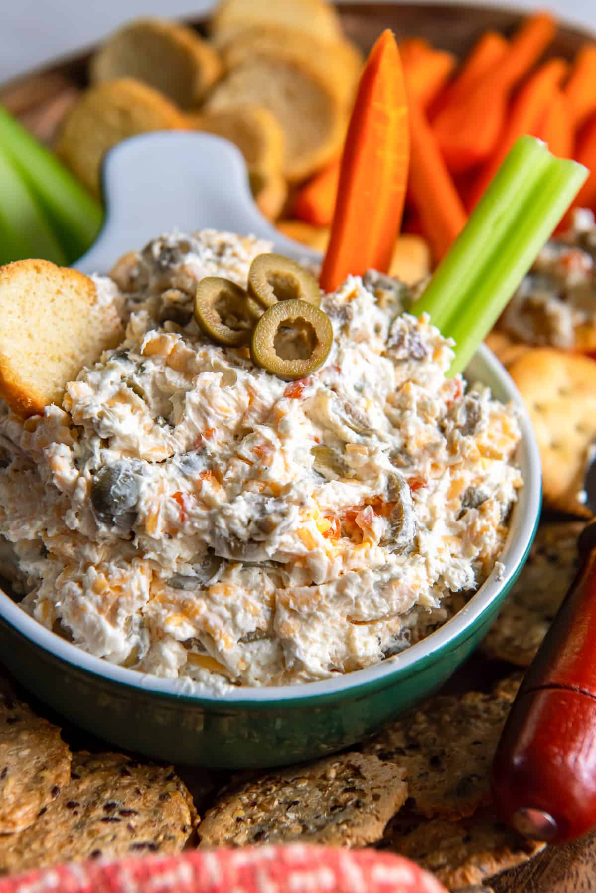 A close up of a carrot and celery stick pressed into a bowl of olive dip.