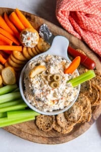 A carrot and celery stick pressing into a bowl of olive dip on a platter.