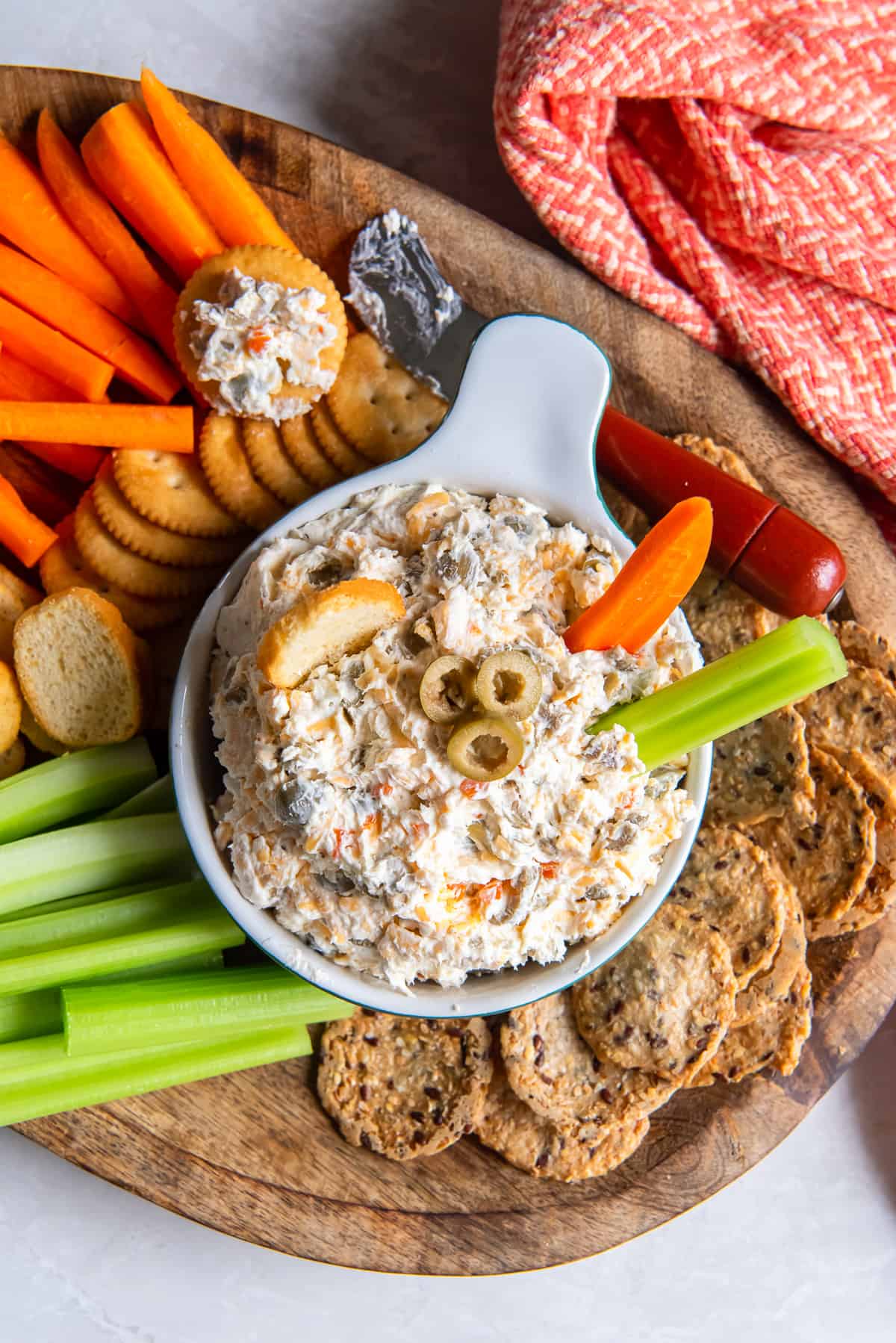 A carrot and celery stick pressing into a bowl of olive dip on a platter.