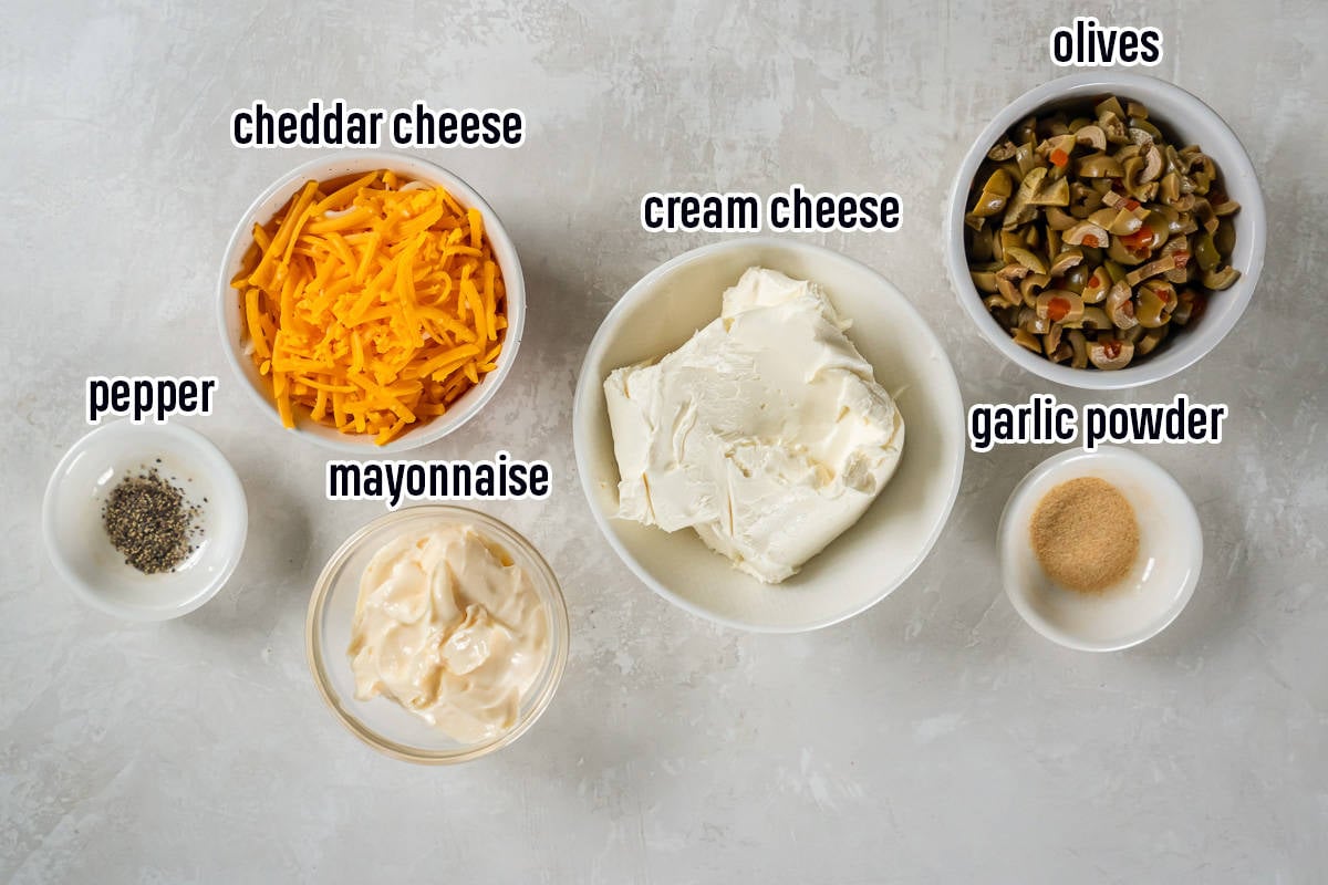Chopped green olives, cream cheese, cheddar cheese and other ingredients in bowls with text.