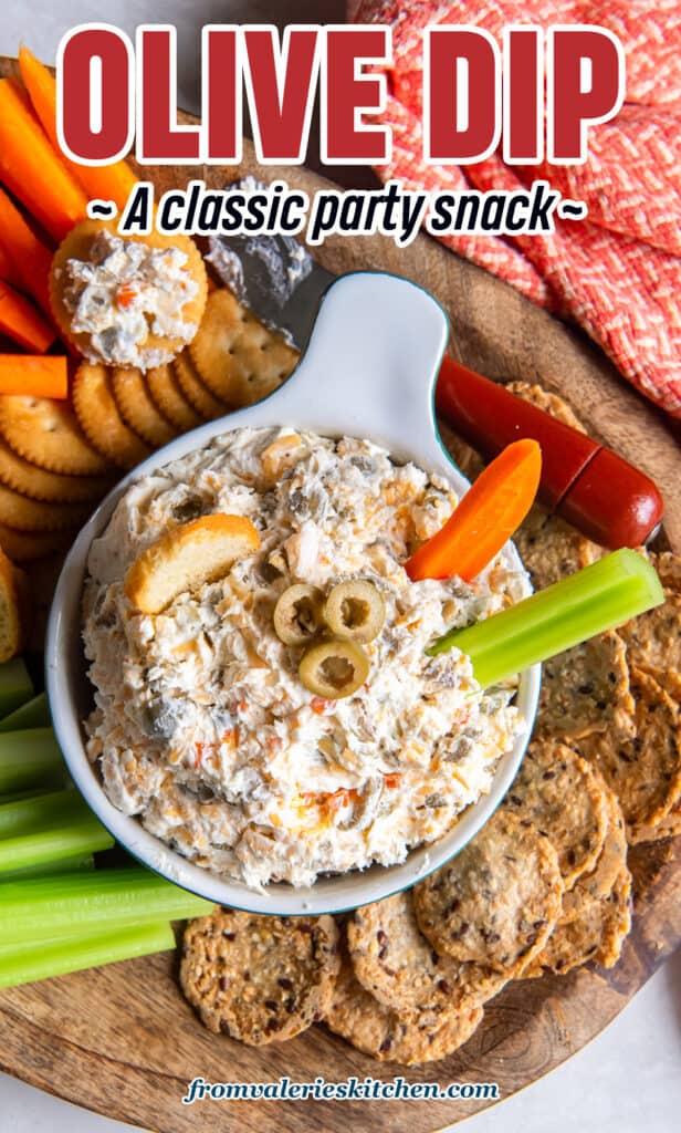 A carrot and celery stick pressing into a bowl of olive dip on a platter with text.