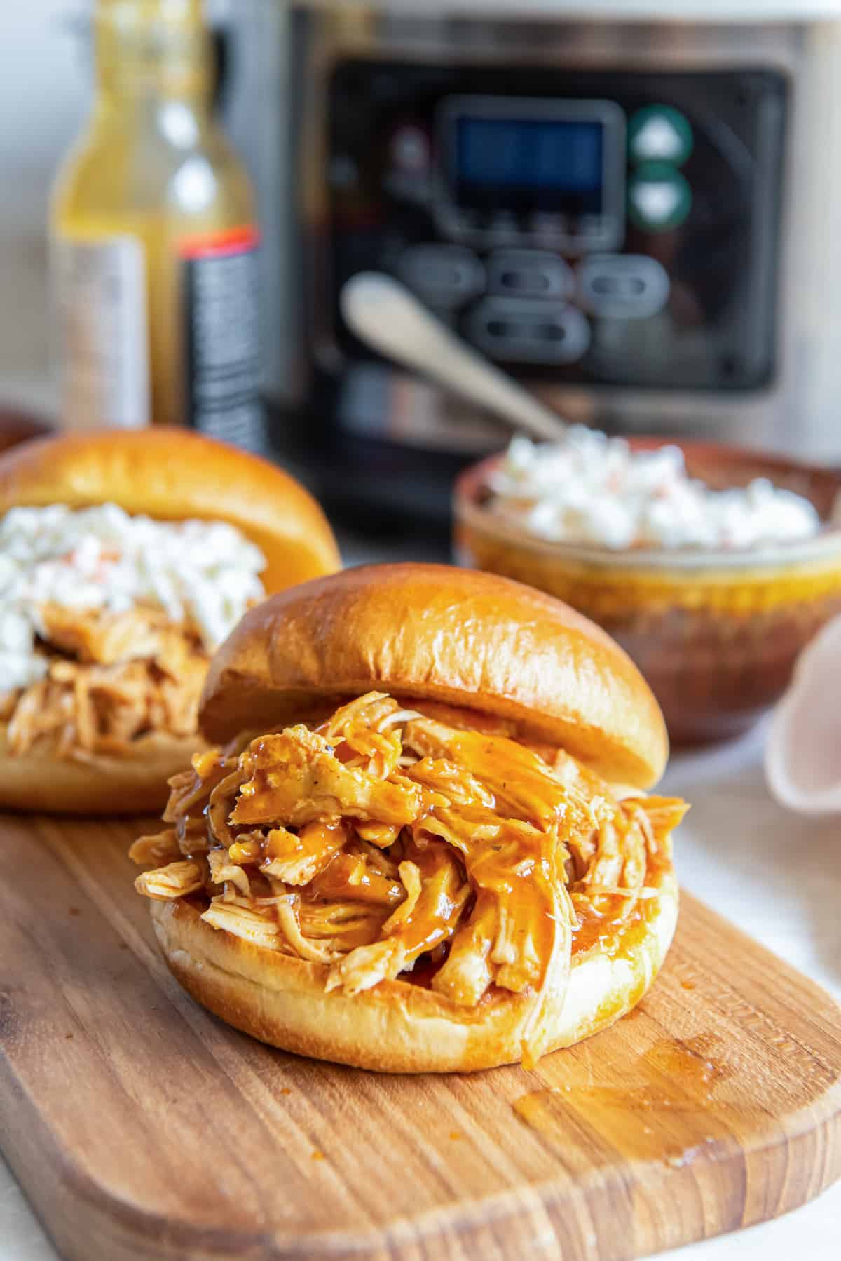 Two small shredded bbq chicken sandwiches on a board in front of a slow cooker.