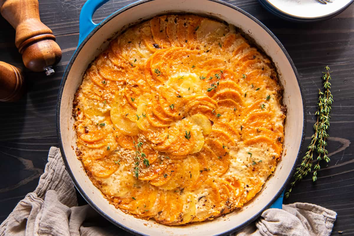 A top down shot of sweet potato gratin topped with fresh thyme in a blue pan.
