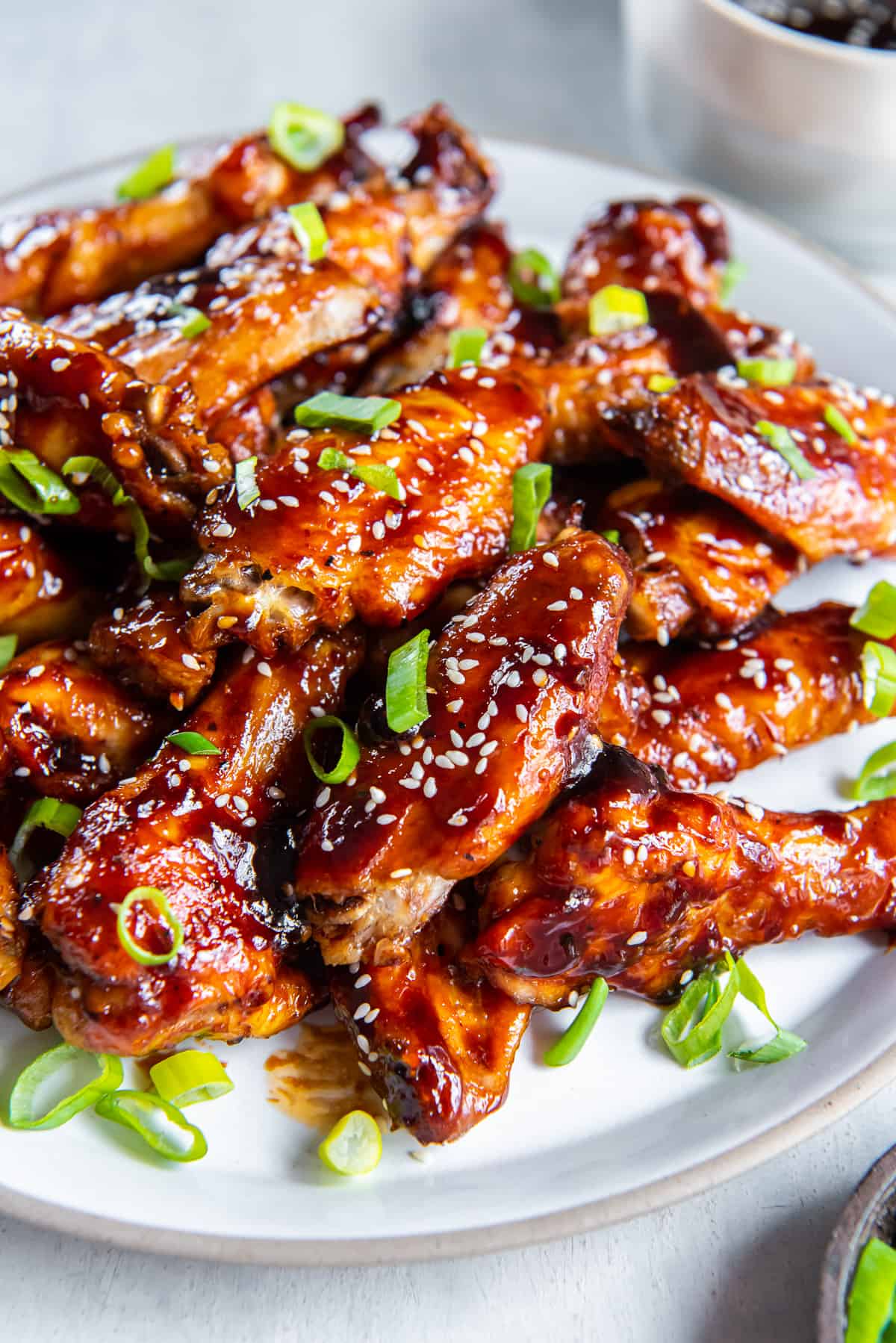Baked Asian chicken wings topped with sesame seeds and green onion piled on a white platter.