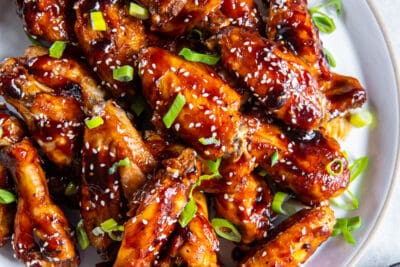 Glazed Asian chicken wings on a platter next to a small bowl of sliced green onions.