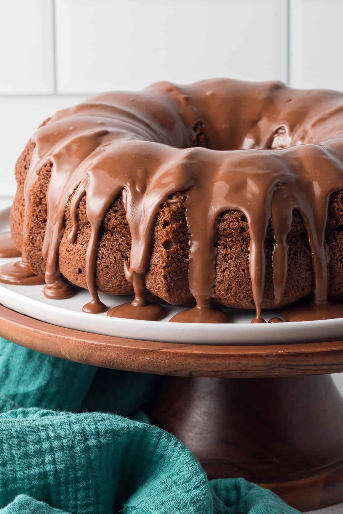 A bundt cake with glaze dripping down the sides on a cake pedestal.
