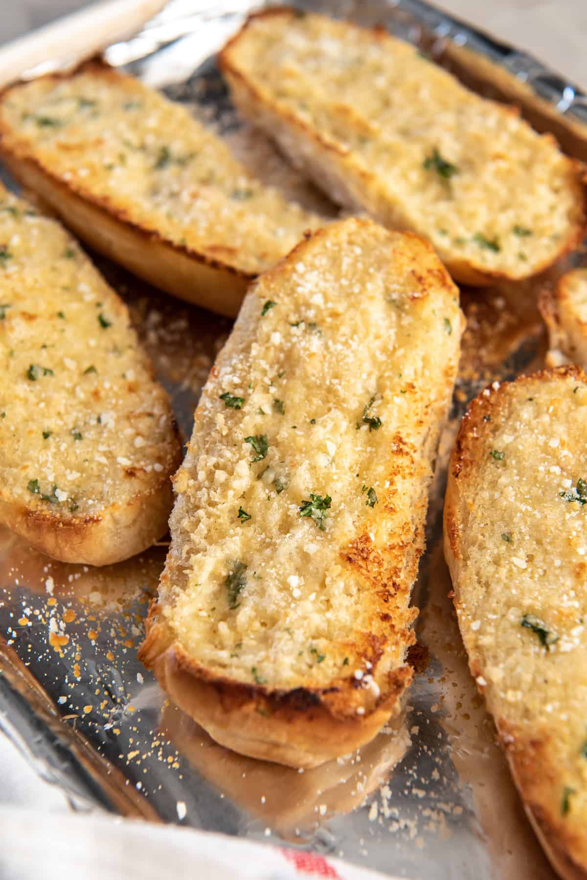 A close up of sandwich roll garlic bread on a foil lined baking sheet.