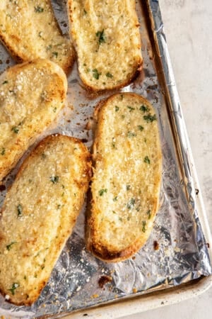 A top down shot of garlic bread made with sandwich rolls on a baking sheet.