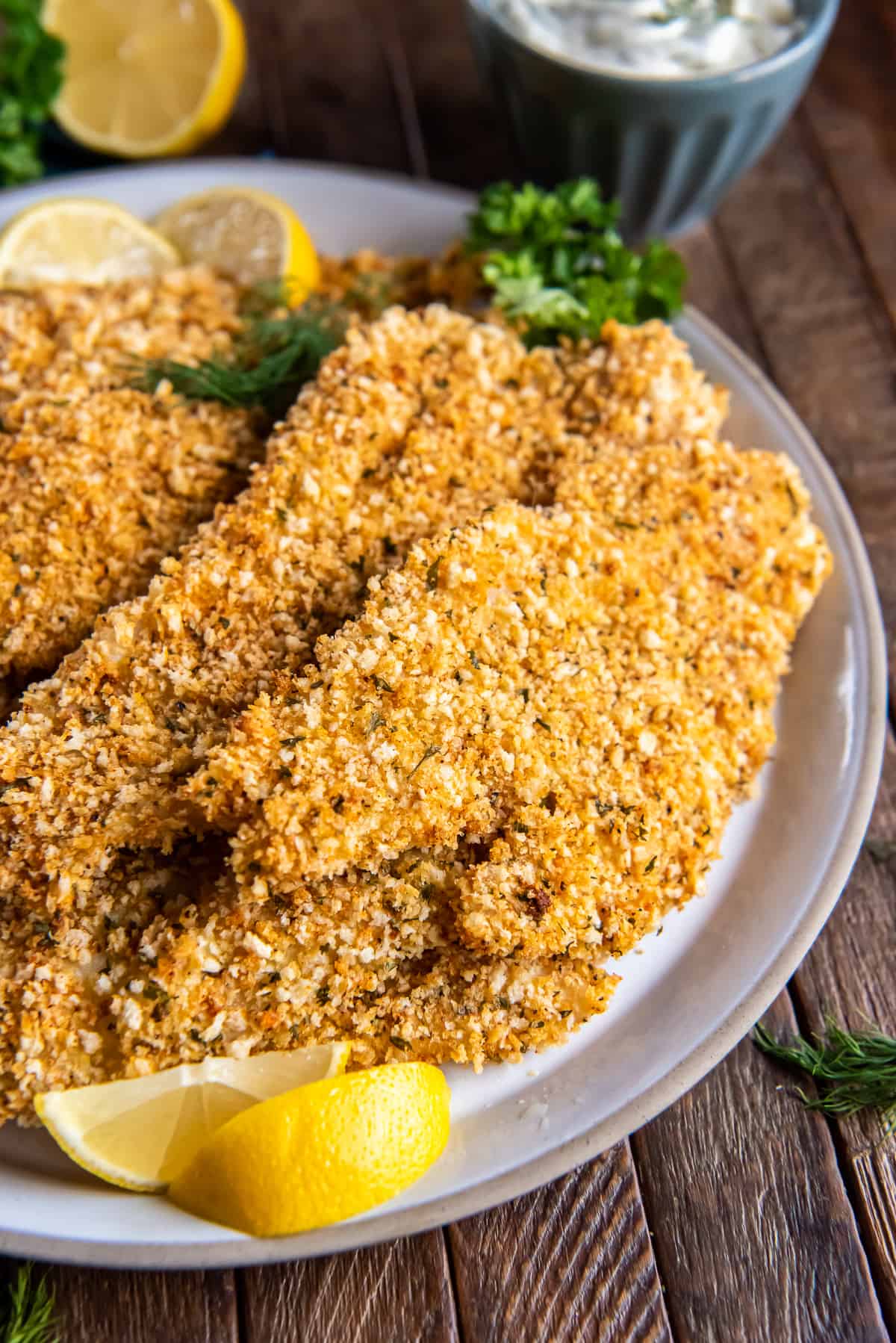 A close up of crispy oven baked fish on a white plate with lemon wedges and fresh dill.