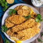 A top down shot of a platter of crispy fish filets next to a small bowl of creamy dill sauce.