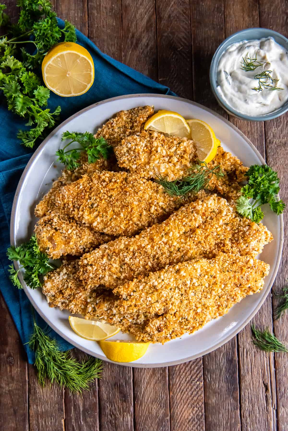 A top down shot of a platter of crispy fish filets next to a small bowl of creamy dill sauce.