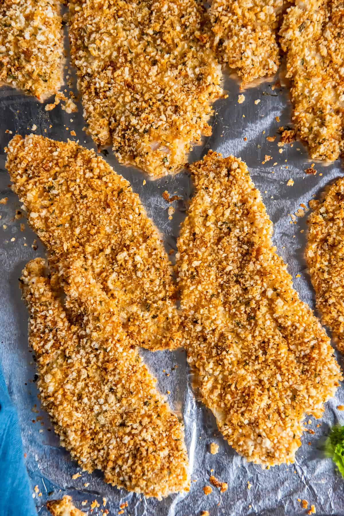 A top down close up shot of crispy baked fish filets on a foil lined baking sheet.