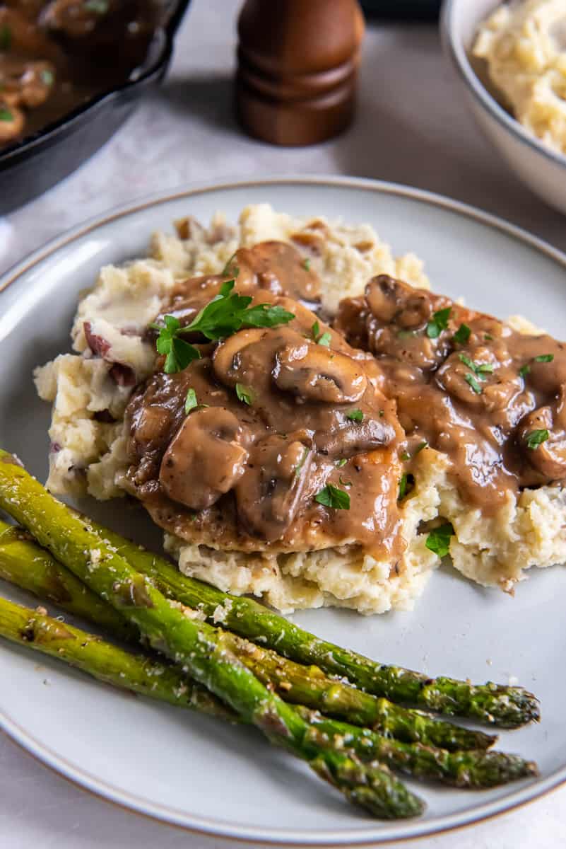 Chicken marsala with mushrooms on a plate with mashed potatoes and asparagus.