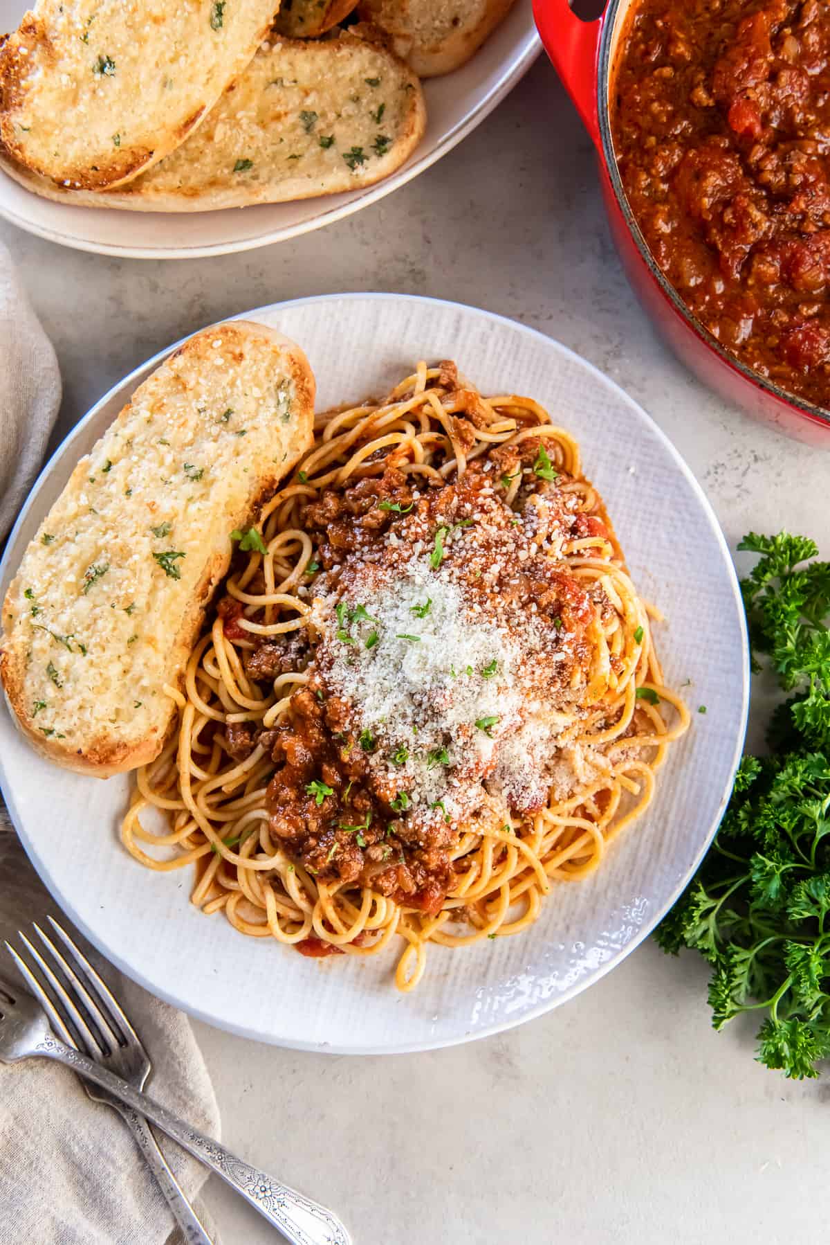 A top down shot of a plate of spaghetti topped with Parmesan cheese on a plate with garlic bread.