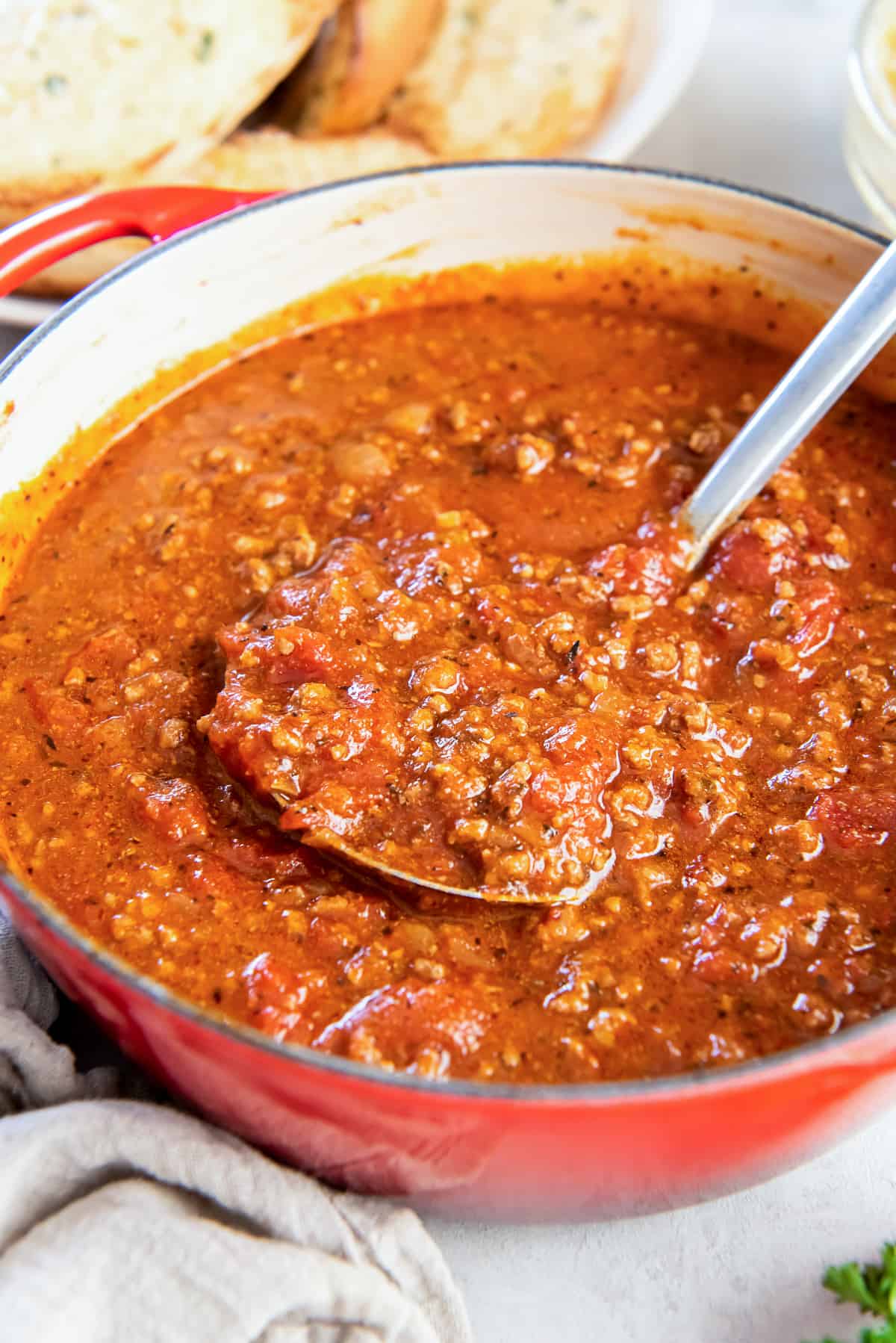 A ladle scooping spaghetti sauce with ground beef from a Dutch Oven.